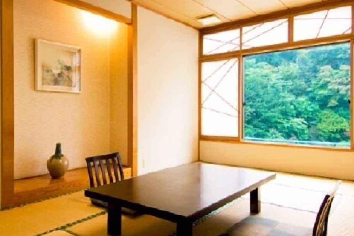 Ein traditioneller japanischer Raum mit Tatami-Boden, einem niedrigen Tisch, einem Stuhl, einer Vase und einem Fenster mit Blick auf Grünflächen.