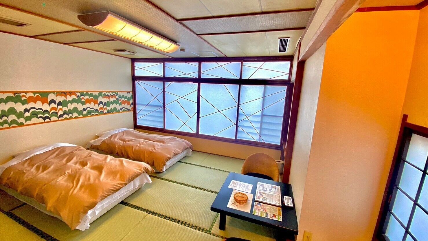 A traditional Japanese room with tatami flooring, two beds with futons, a shoji screen window, and a small table with a menu.