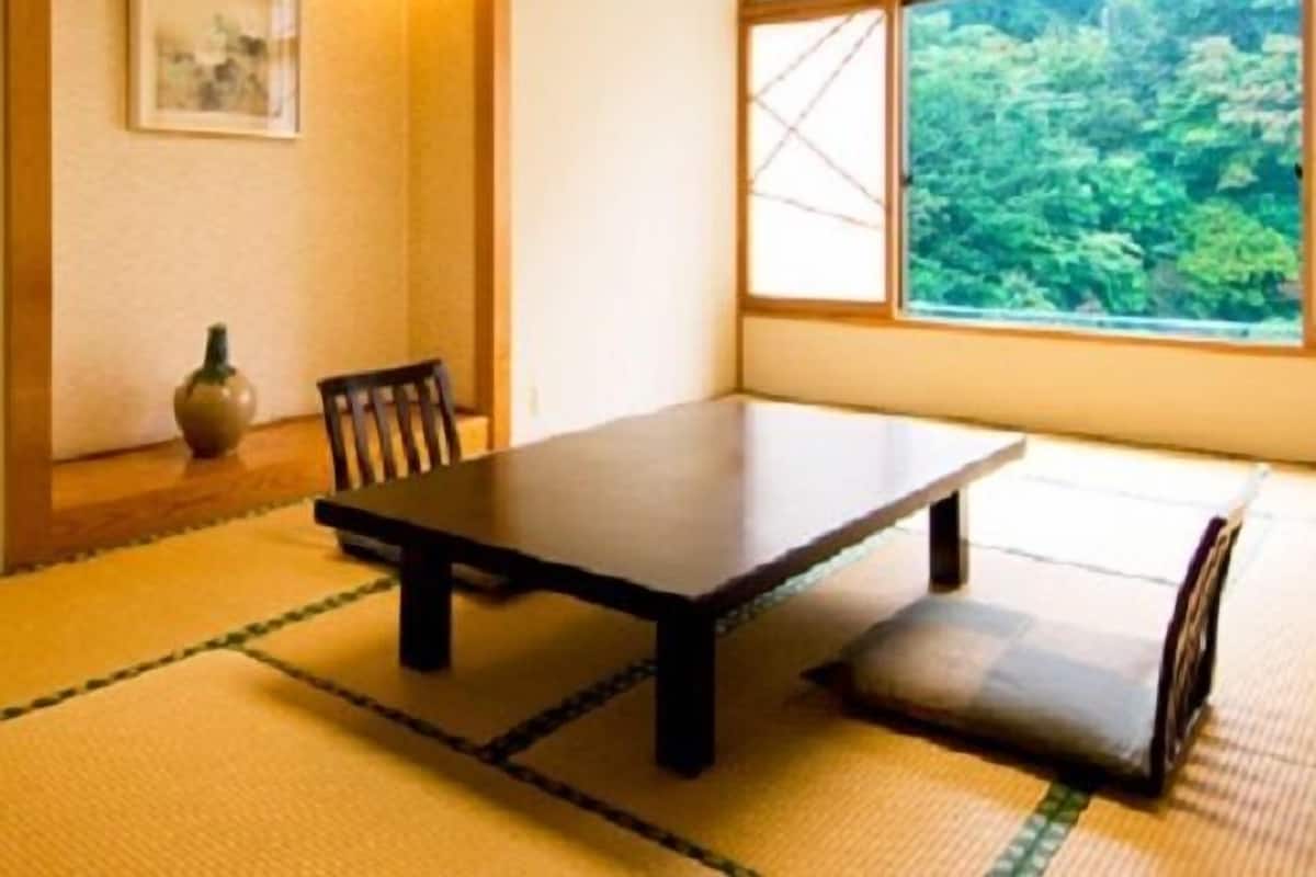 Ein traditioneller japanischer Raum mit Tatami-Boden, einem niedrigen Tisch, einem Stuhl, einer Vase und einem Fenster mit Blick auf Grünflächen.