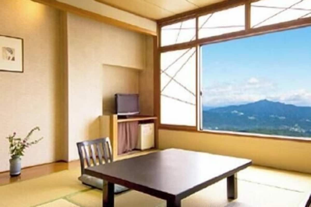 Ein Zimmer mit großem Fenster, einem Tisch, einem Stuhl, einem Fernseher und einer kleinen Pflanze.