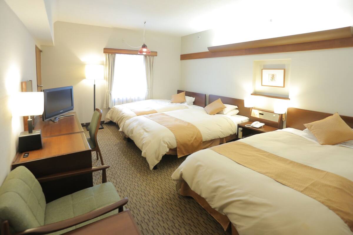 Habitación de hotel con dos camas, un escritorio con televisor, una silla y una mesita de noche con lámpara.