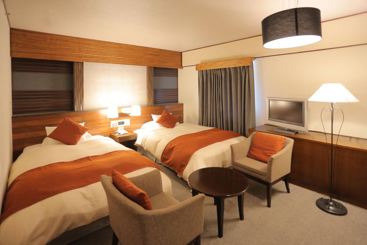 Habitación de hotel con dos camas, un televisor, un escritorio, una silla y una lámpara.