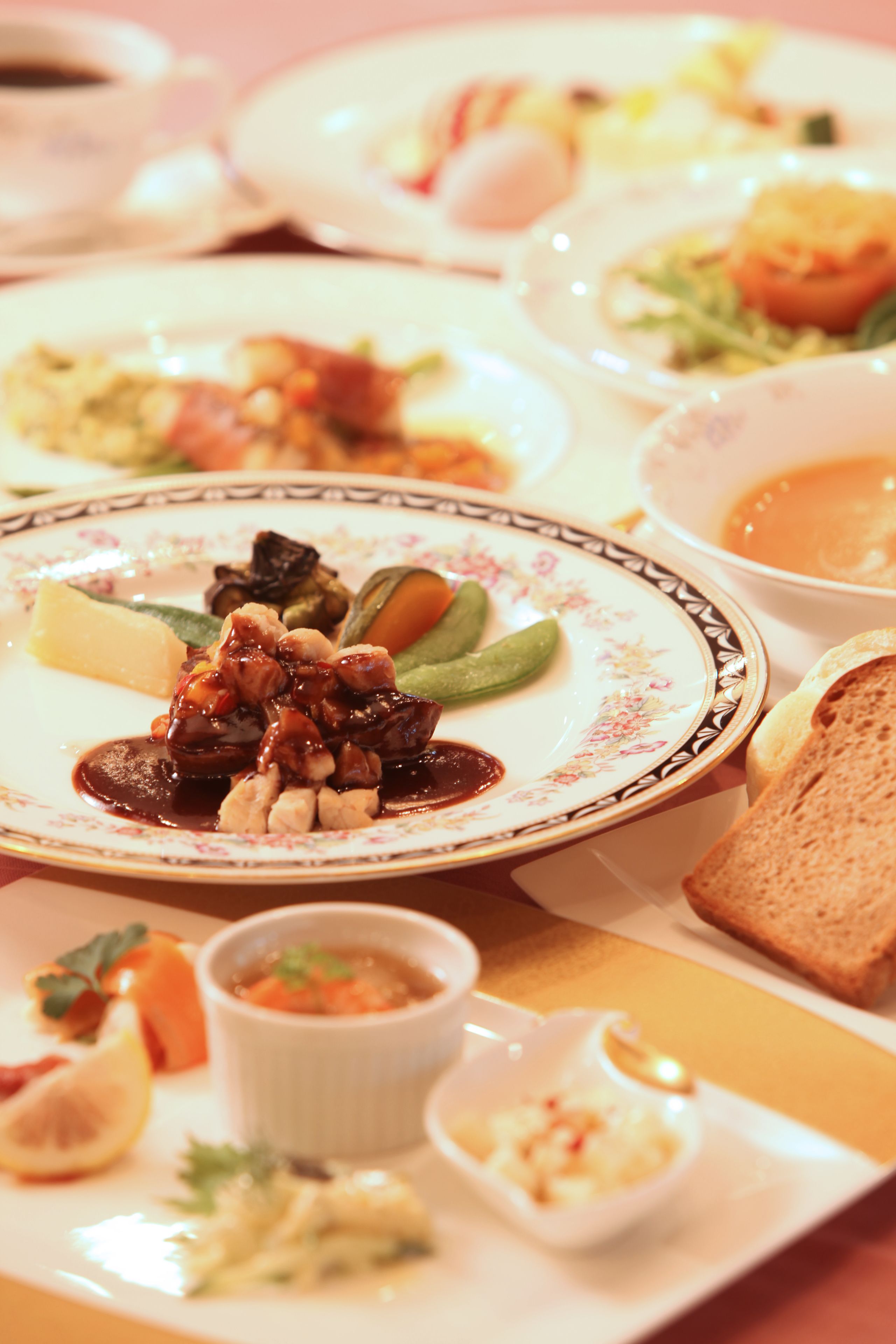 A variety of dishes on a table, including a plate with meat and vegetables, a bowl of soup, and a slice of bread.