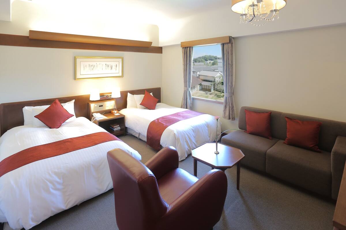Habitación de hotel con dos camas, un sofá, una silla, una mesita y un candelabro.