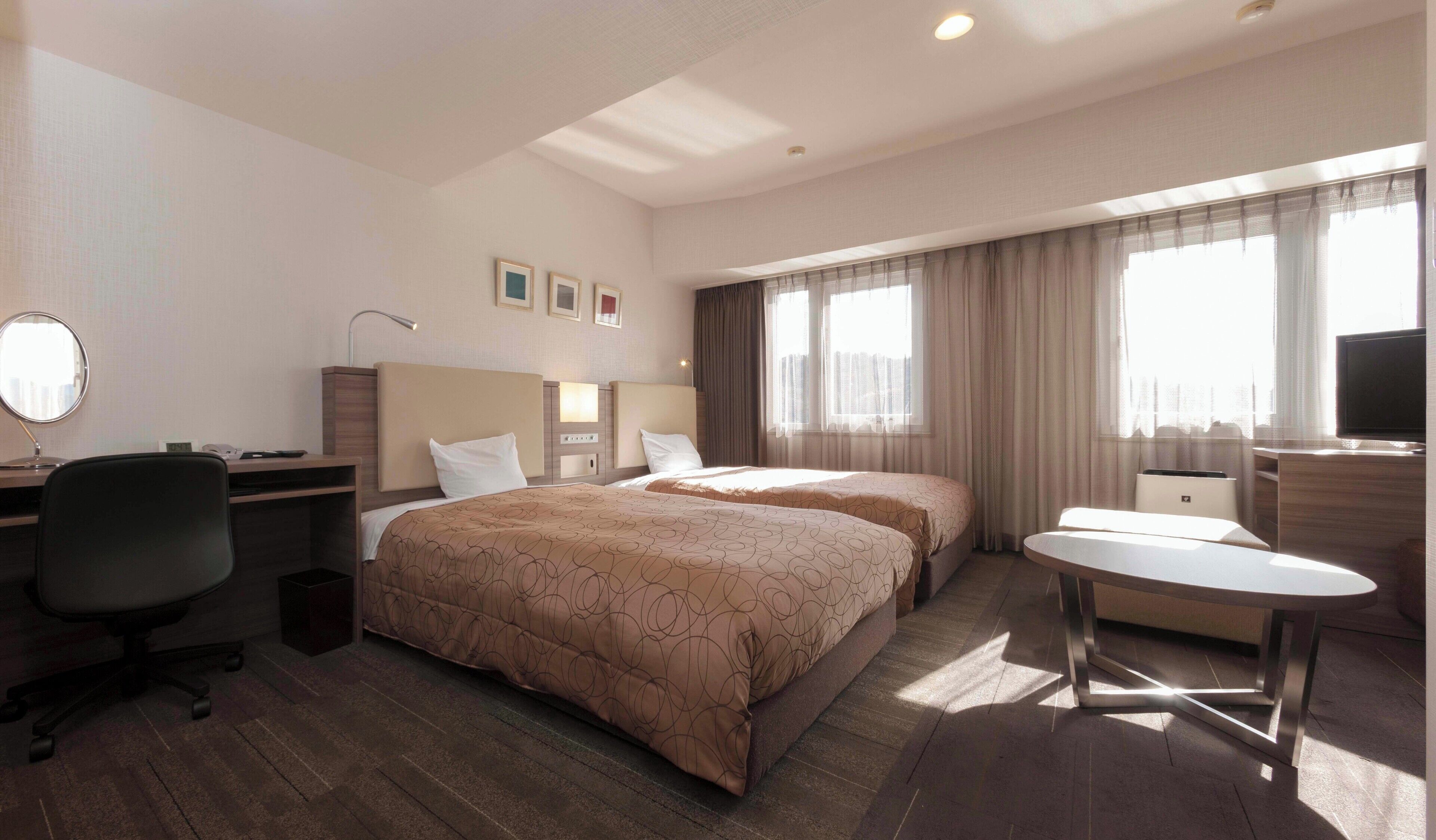 A hotel room with two beds, a desk with a chair, a TV, and a small table.