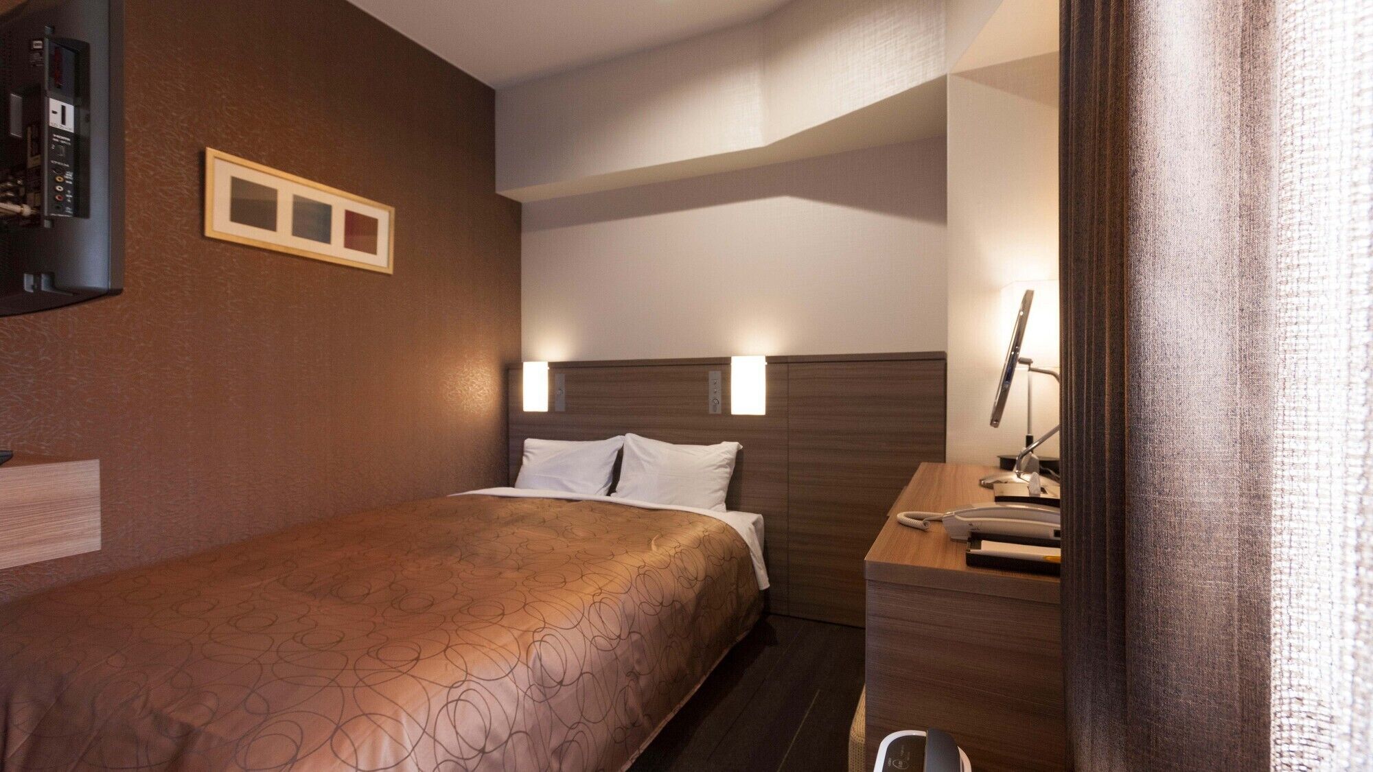 A hotel room with a bed, bedside table, lamp, and a framed picture on the wall.