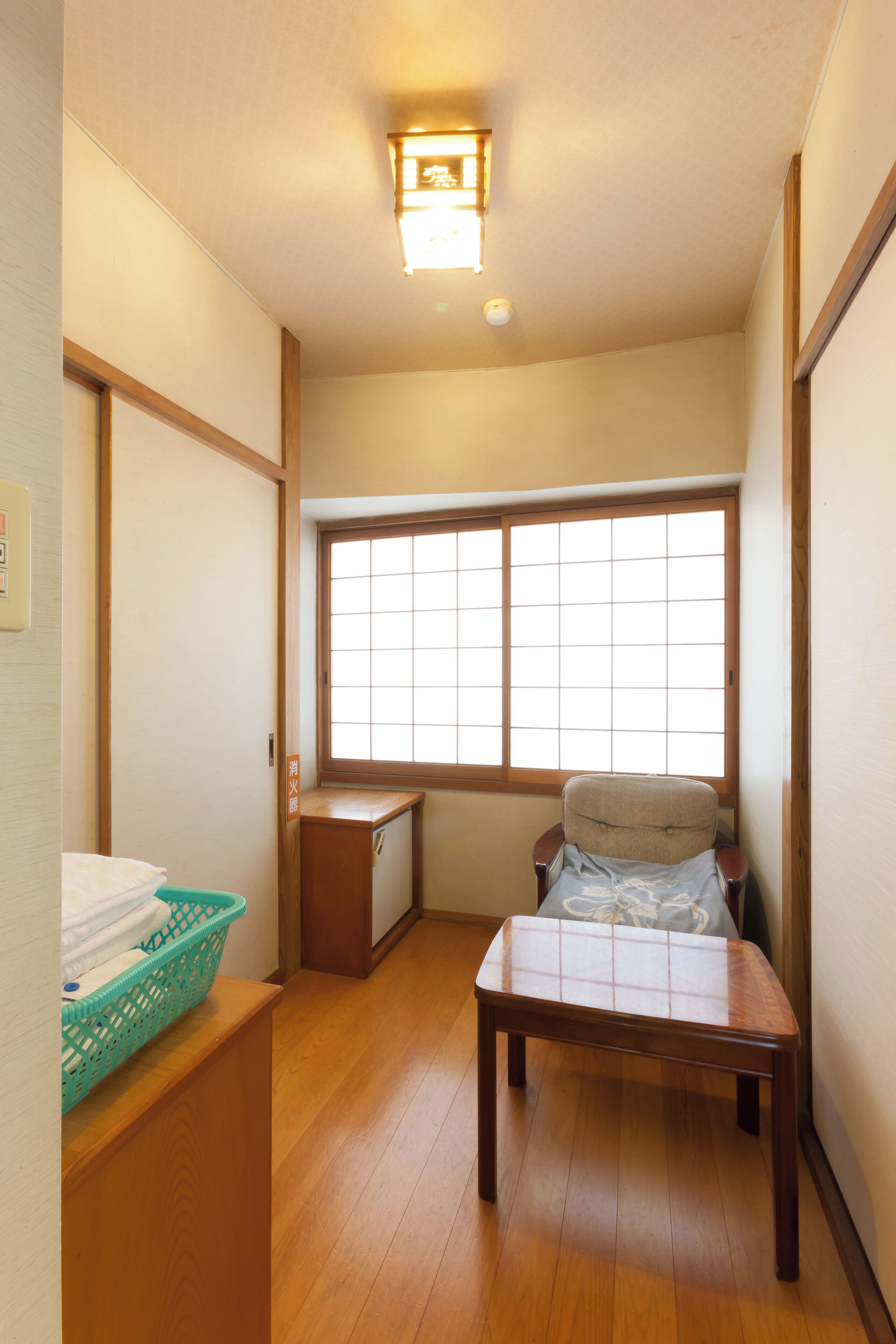 Una habitación japonesa tradicional con suelo de tatami, una mesa de madera baja, una silla acolchada y un ventanal con celosías shoji.