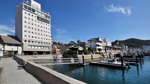 A waterfront hotel with a modern design, featuring a prominent sign, a dock with boats, and a clear view of the water. - Onomichi Royal Hotel (Onomichi)