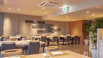 A modern dining area with multiple tables and chairs, a wall-mounted light fixture, and a visible exit sign.