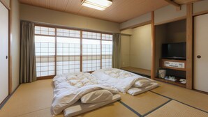 A traditional Japanese-style room with tatami flooring, a futon bed, sliding doors, and a television on a wooden shelf. - Onomichi Royal Hotel (Onomichi)