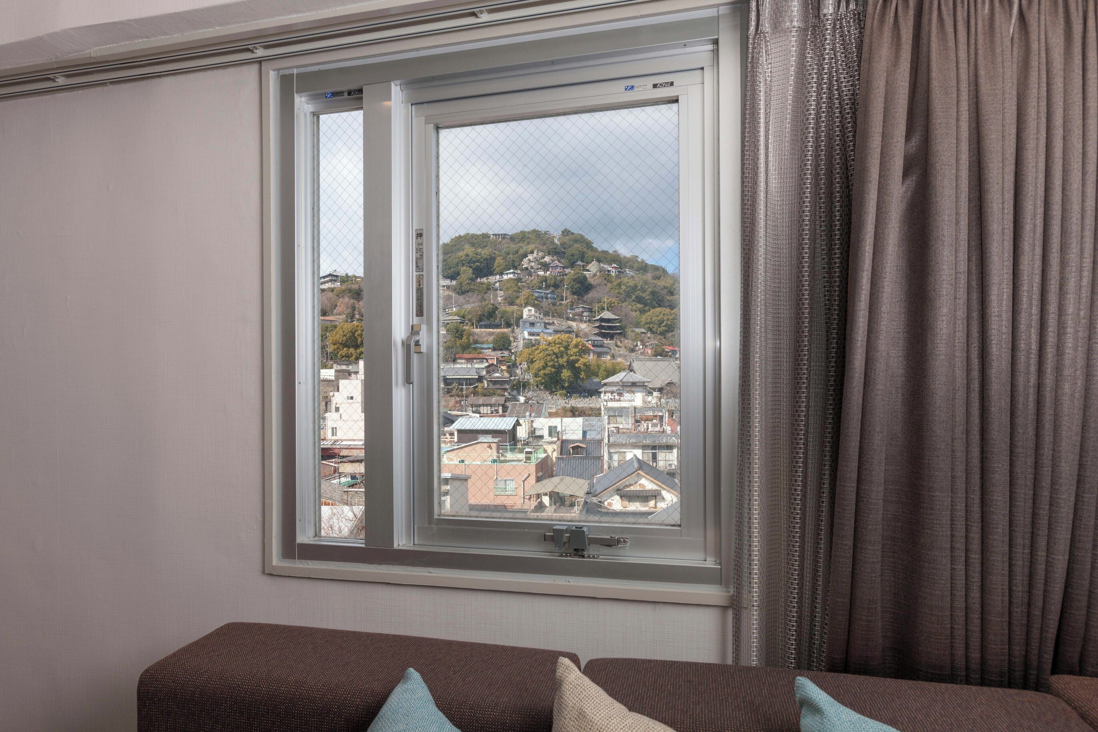 A room with a large window offering a view of a cityscape and hills.