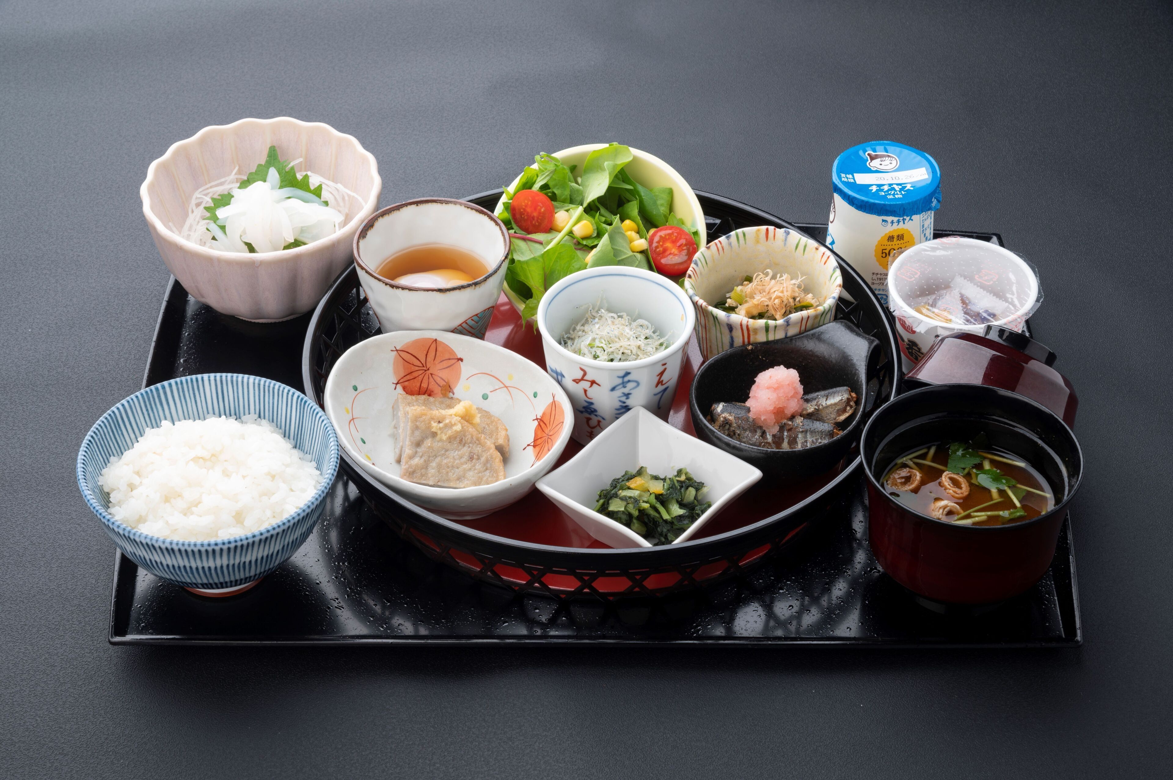 Un repas japonais traditionnel, composé de différents plats, servis sur un plateau noir.