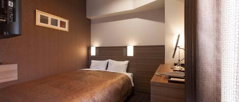 Una habitación de hotel con cama, mesita de noche, lámpara y un escritorio pequeño con una silla.