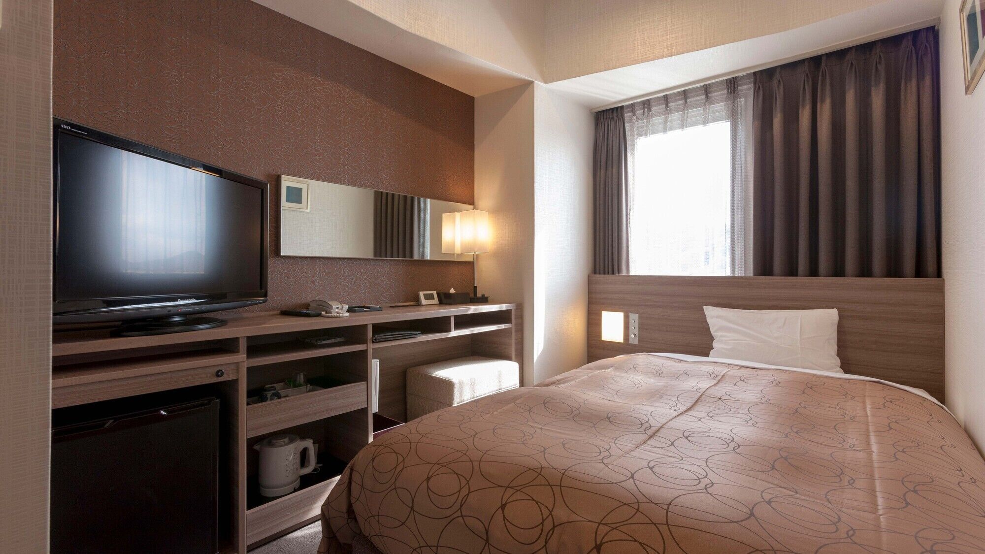 A hotel room with a TV, bedside table, lamp, and a bed with a patterned bedspread.