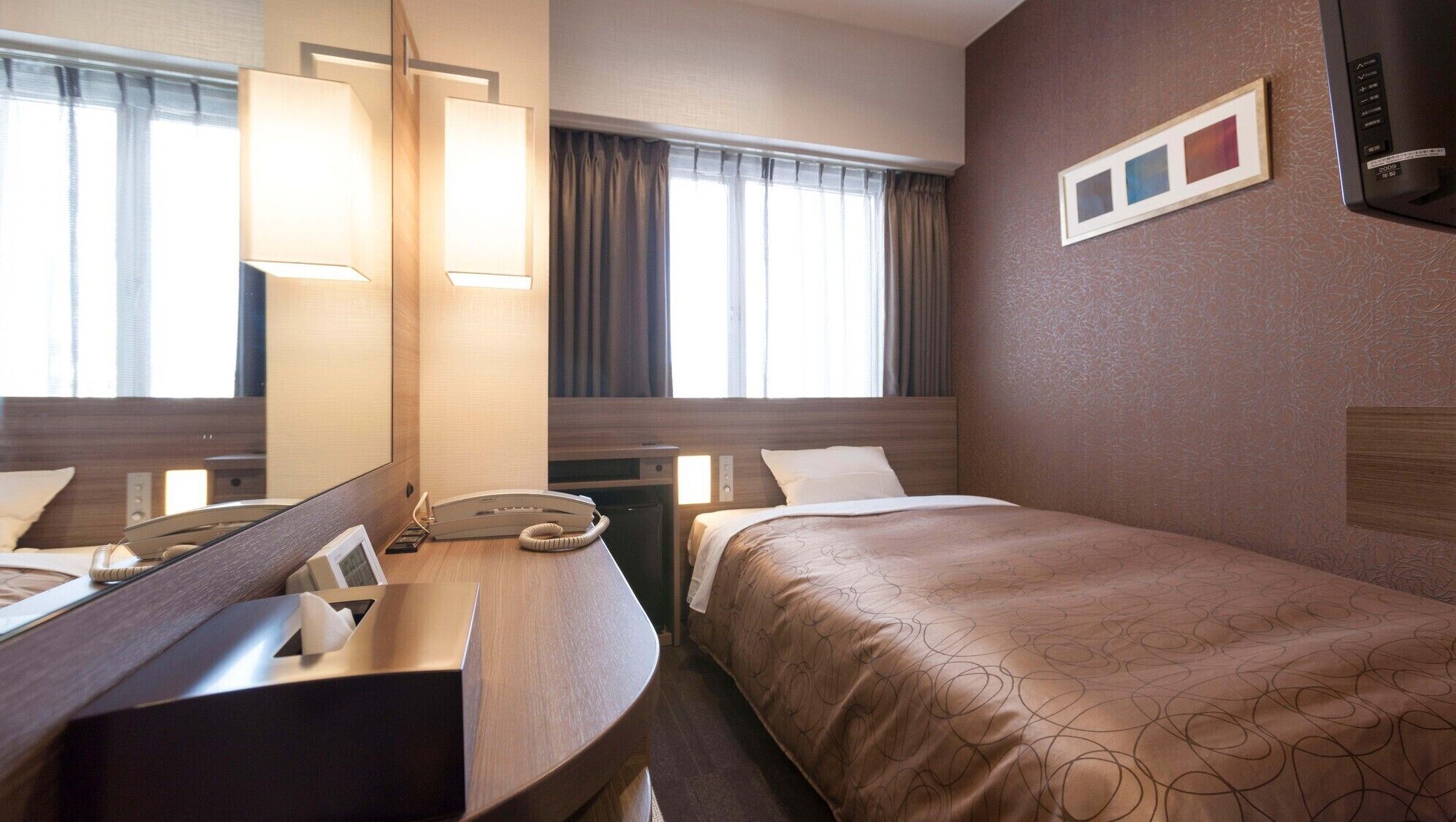 A hotel room with a bed, bedside table, lamp, telephone, and a mirror.