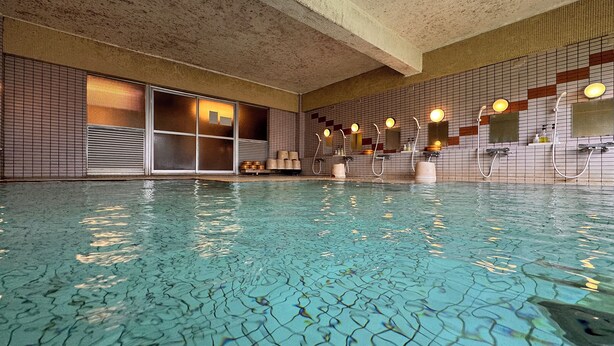 An indoor swimming pool with tiled walls, a window with blinds, and multiple showerheads. - Kidoike Onsen Hotel (Yamanouchi)
