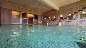 An indoor swimming pool with tiled walls, a window with blinds, and multiple showerheads. - Kidoike Onsen Hotel (Yamanouchi)