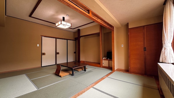 A traditional Japanese room with tatami flooring, a low table, sliding doors, and a wooden wardrobe. - Kidoike Onsen Hotel (Yamanouchi)