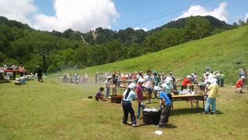 A group of people gathered outdoors, possibly at a picnic or event, with tables and cooking equipment visible.