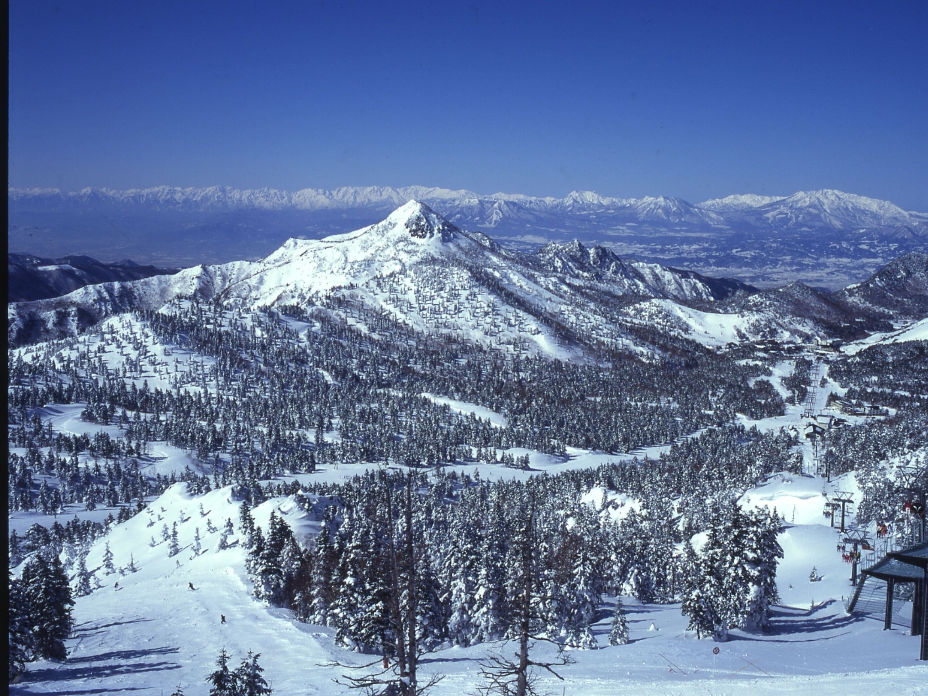 Paisaje montañoso cubierto de nieve con pistas de esquí y un telesilla.