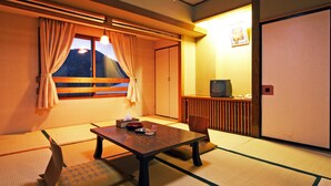 A traditional Japanese room with tatami flooring, a low table, a cushioned bench, a television, and a sliding door. - Kidoike Onsen Hotel (Yamanouchi)