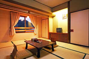Traditional Japanese-style room with tatami flooring, low table, and sliding door leading to another room.