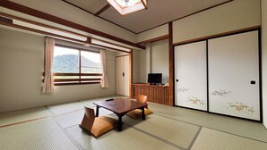 A traditional Japanese room with tatami flooring, a low table, cushions, a television, and sliding doors. - Kidoike Onsen Hotel (Yamanouchi)