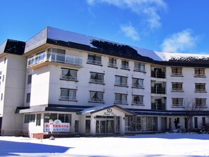 Experience the serene atmosphere of this hotel, featuring a central entrance with a glass door and a sign above it, surrounded by multiple balconies with metal railings.