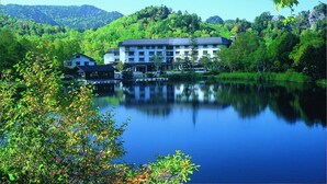 A large building with multiple floors, surrounded by lush greenery and a calm lake. - Kidoike Onsen Hotel (Yamanouchi)