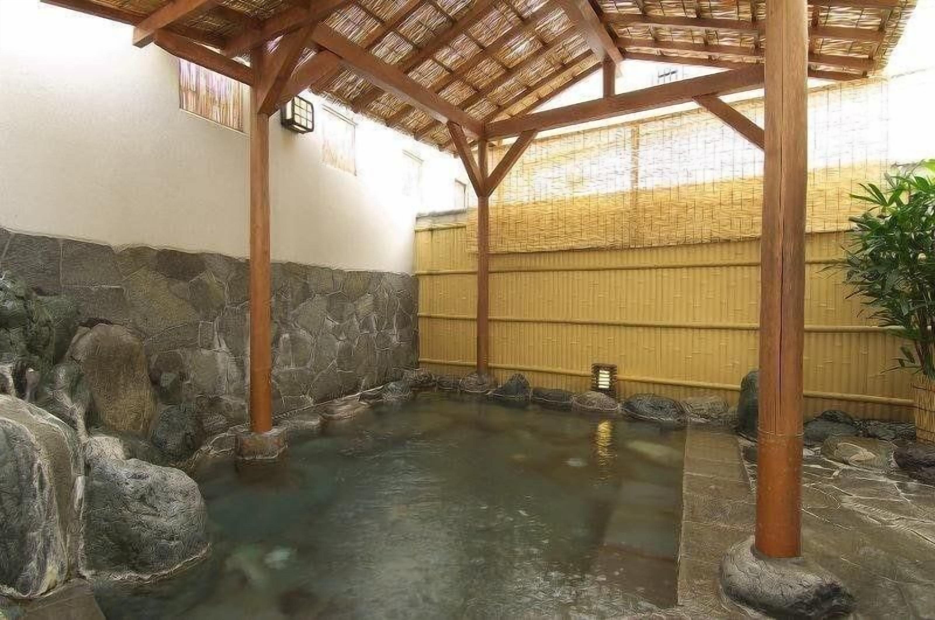 Un onsen japonès tradicional amb una banyera de pedra, pilars de fusta i una tanca de bambú.