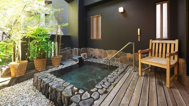 A hot tub surrounded by stone walls, wooden deck, and potted plants. - Onyado Megumi (Yugawara)
