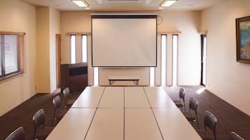 Ein Konferenzraum mit einem langen Tisch, Stühlen, einer Projektionsleinwand und Fenstern.