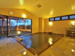 A hot spring bath with a glass enclosure, a clock, and a view of a building outside. - Onyado Megumi (Yugawara)