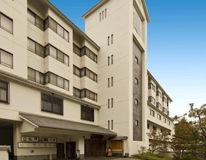 A multi-story hotel with a central entrance, balconies on each floor, and a clock tower. - Onyado Megumi (Yugawara)