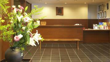 Uma área de recepção com um banco de madeira, um vaso de flores e um painel com certificados.