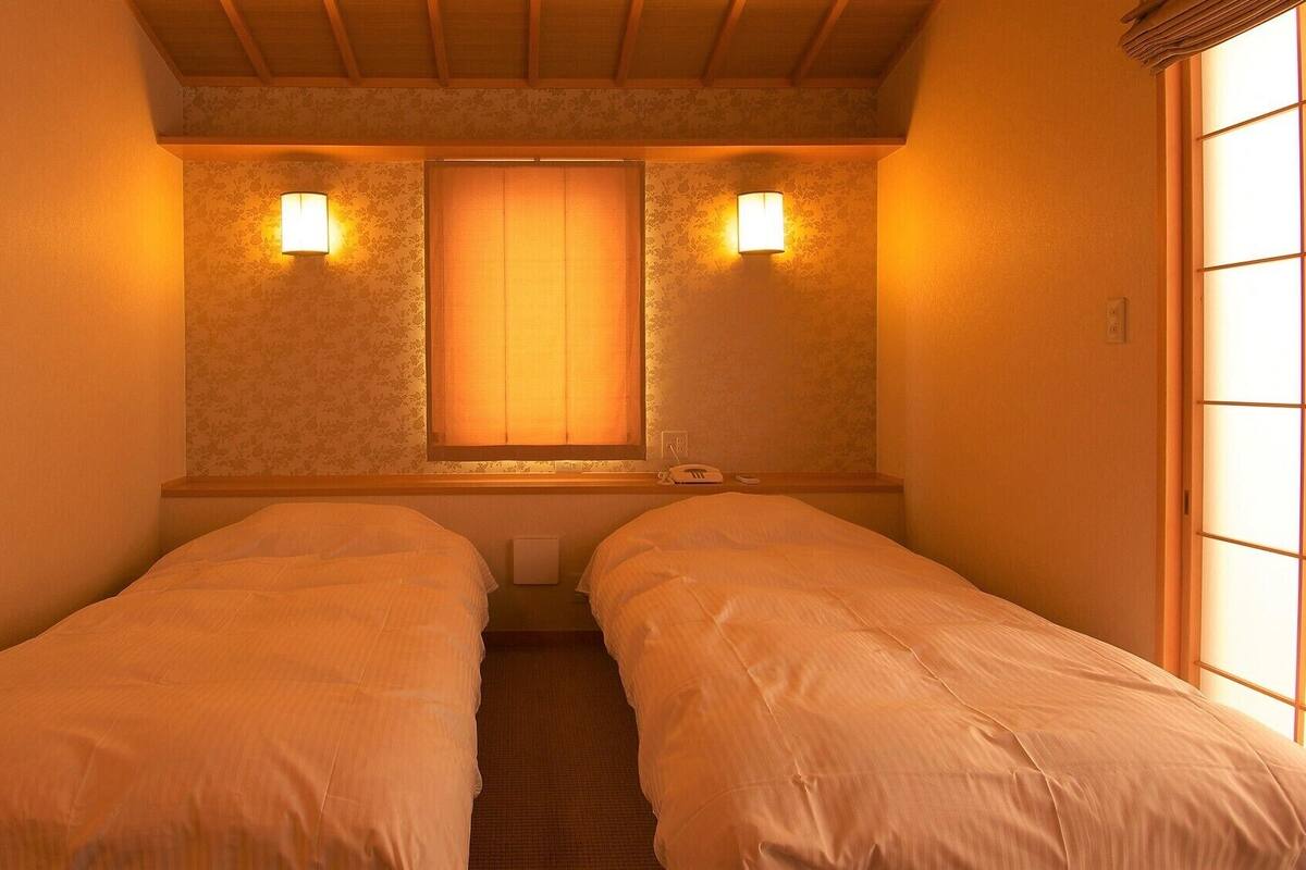 Quarto com duas camas, janela com vista e luminárias na parede.