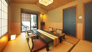 A traditional Japanese room with tatami flooring, a low table with cushions, a television, and sliding doors. - Onyado Megumi (Yugawara)