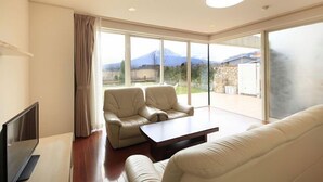 Amplia sala de estar con un ventanal, televisor de pantalla plana, dos sofás de cuero y una mesa de centro de madera.