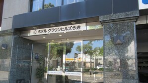 Entrada de un hotel con puertas de vidrio, un letrero en japonés y un felpudo verde.