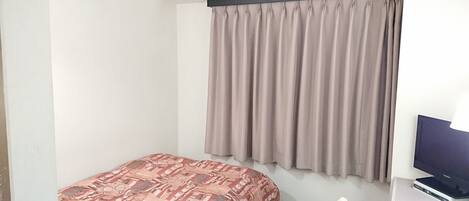 A small, simple room with a bed, a desk, a chair, and a TV.