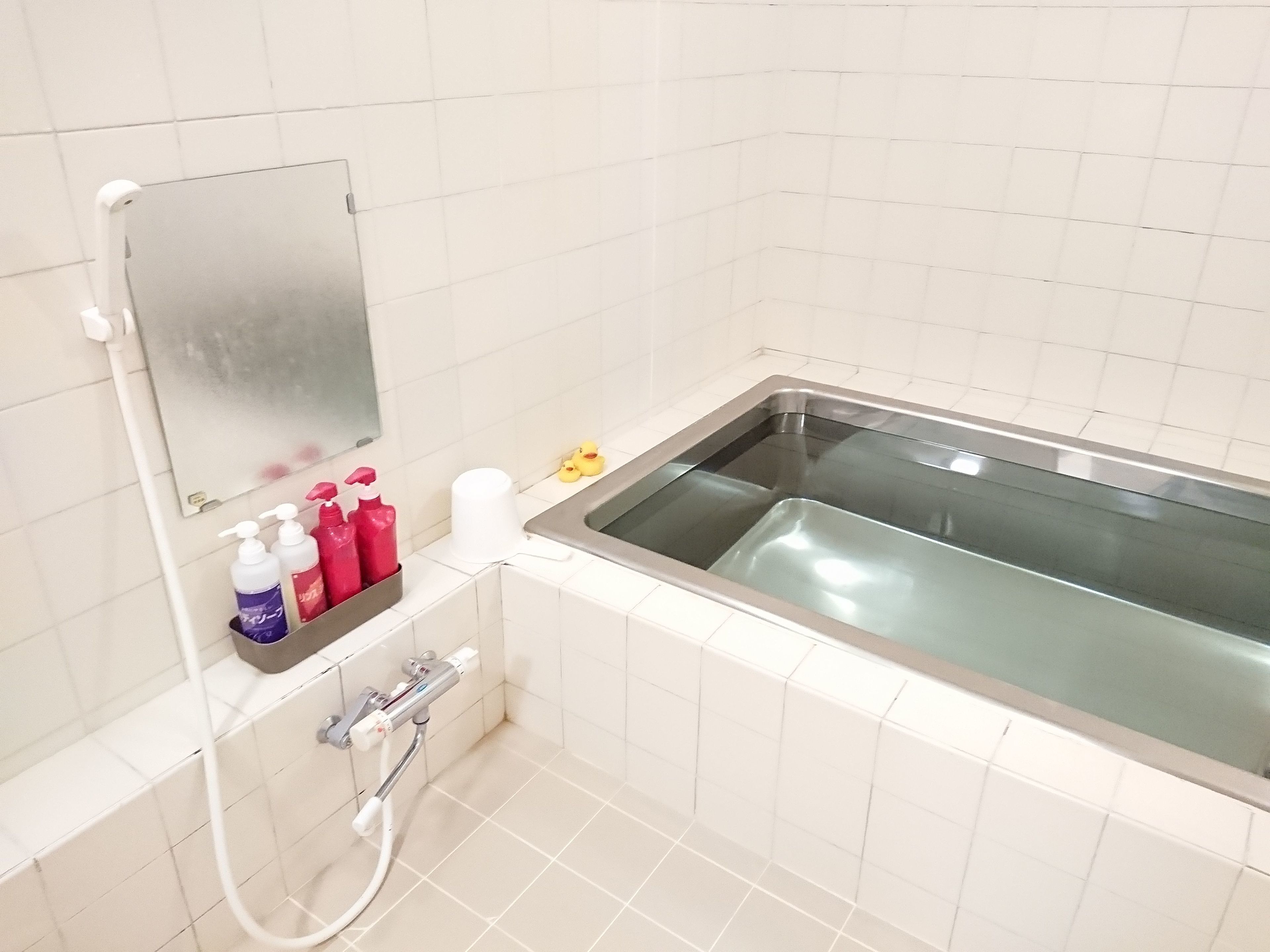 A bathroom with a bathtub, a mirror, and a shelf with toiletries.