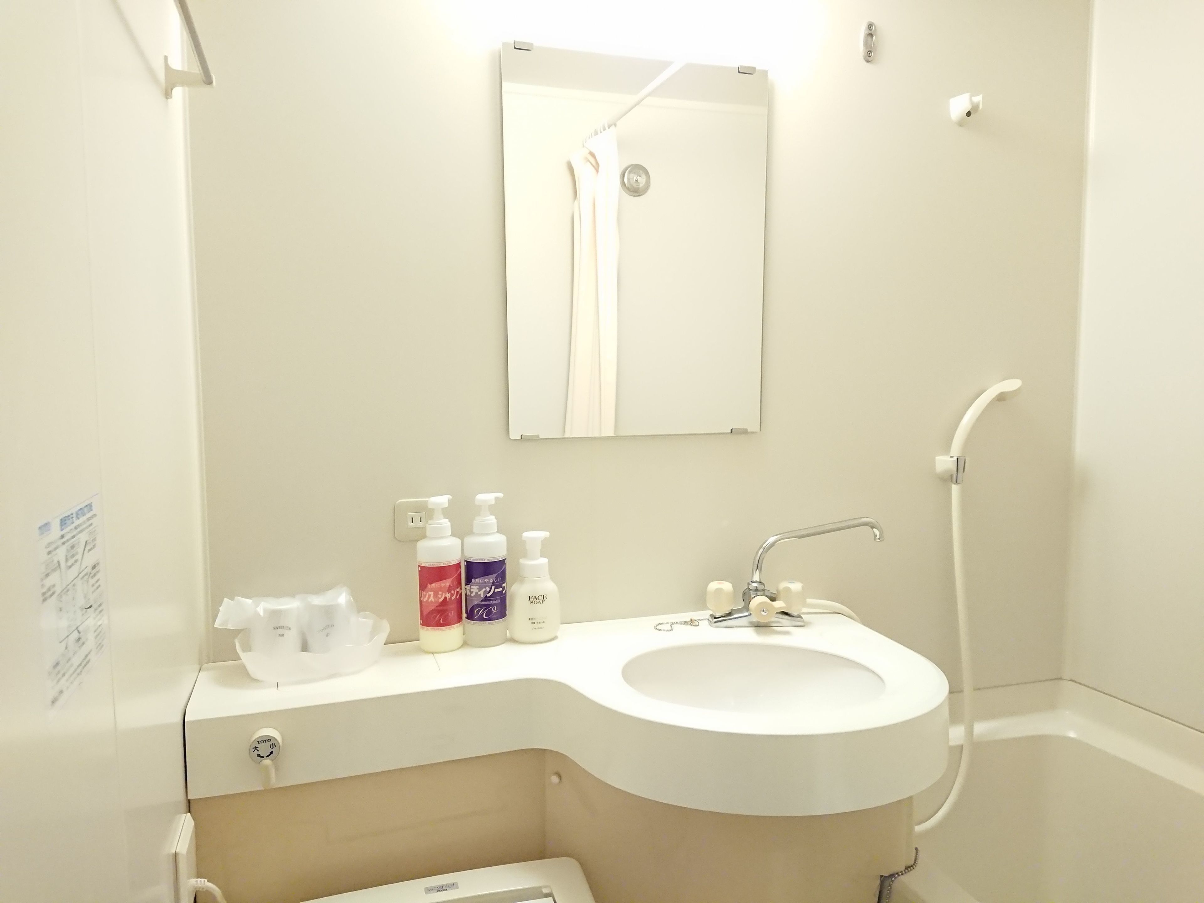 A bathroom with a white sink, a mirror, and a shower. There are toiletries on the counter.