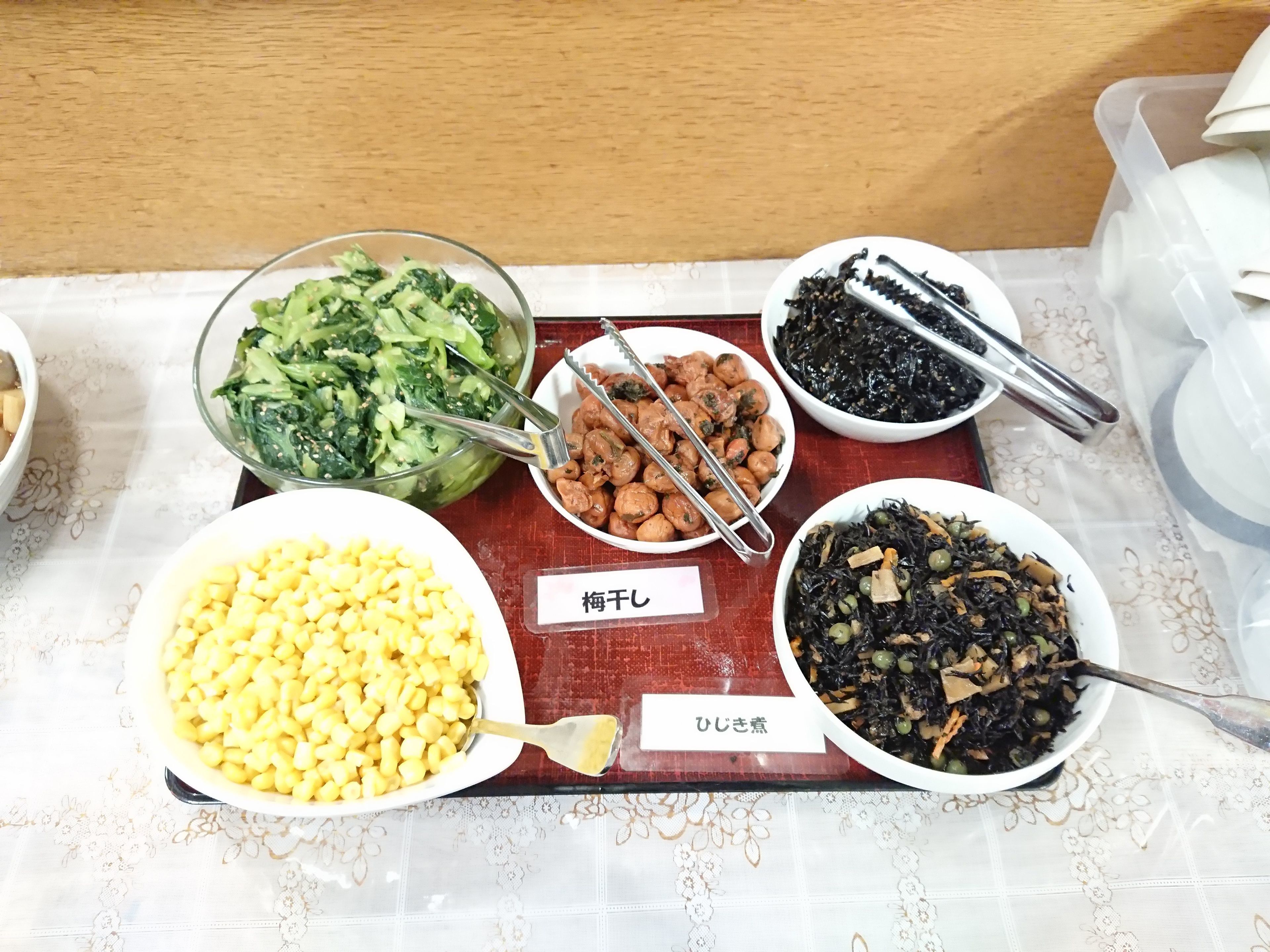 Une table où l’on peut voir différents plats, notamment un bol de maïs, un plat de légumes verts et une assiette de champignons.