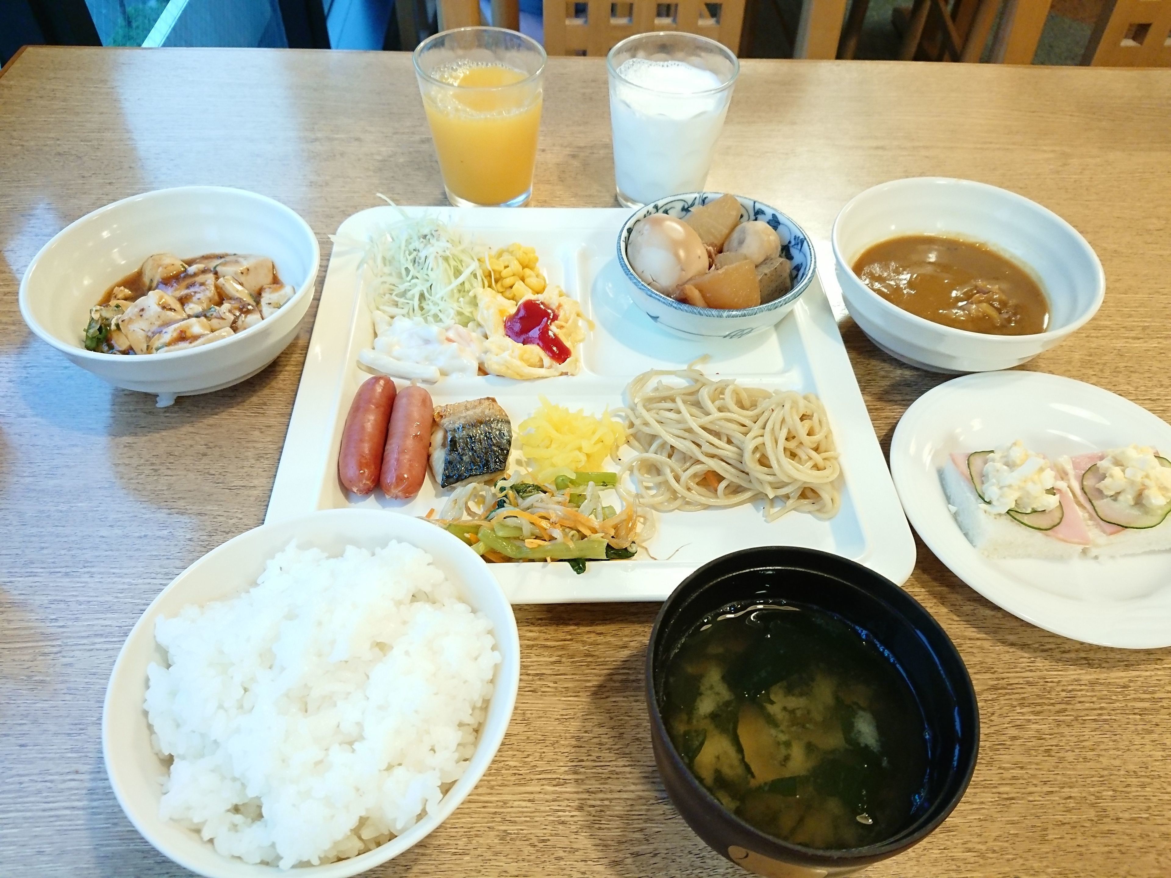 A meal with various dishes including rice, noodles, and soup on a wooden table.