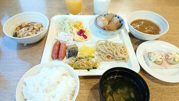 A meal with various dishes including rice, noodles, and soup on a wooden table.