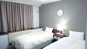 Habitación de hotel con dos camas, una mesita de noche con lámpara, un reloj en la pared y una ventana con cortinas.