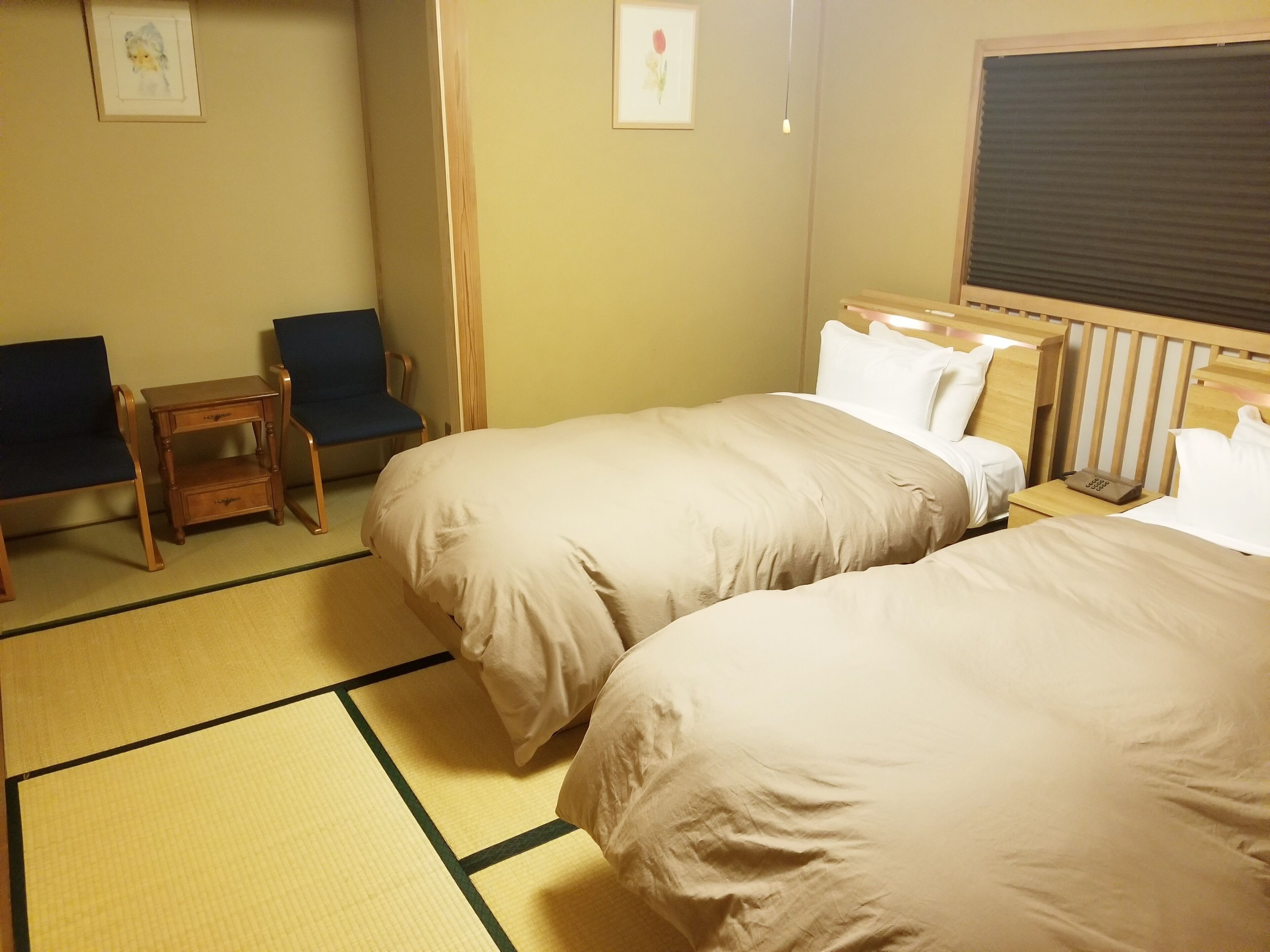 A hotel room with two beds, a small table, a chair, and a futon.
