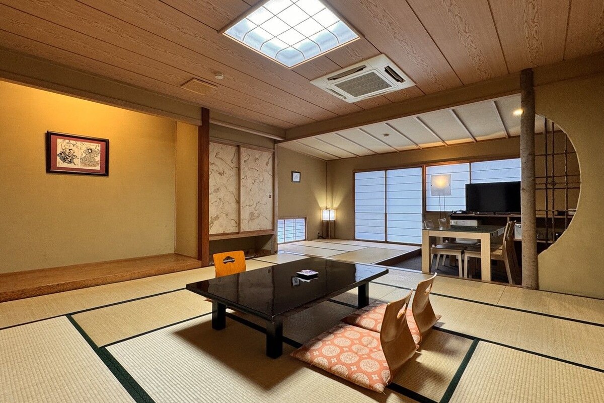 A traditional Japanese room with tatami flooring, a low table, cushions, and a television.