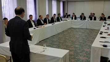 A conference room with a long table, chairs, and a speaker at the front.
