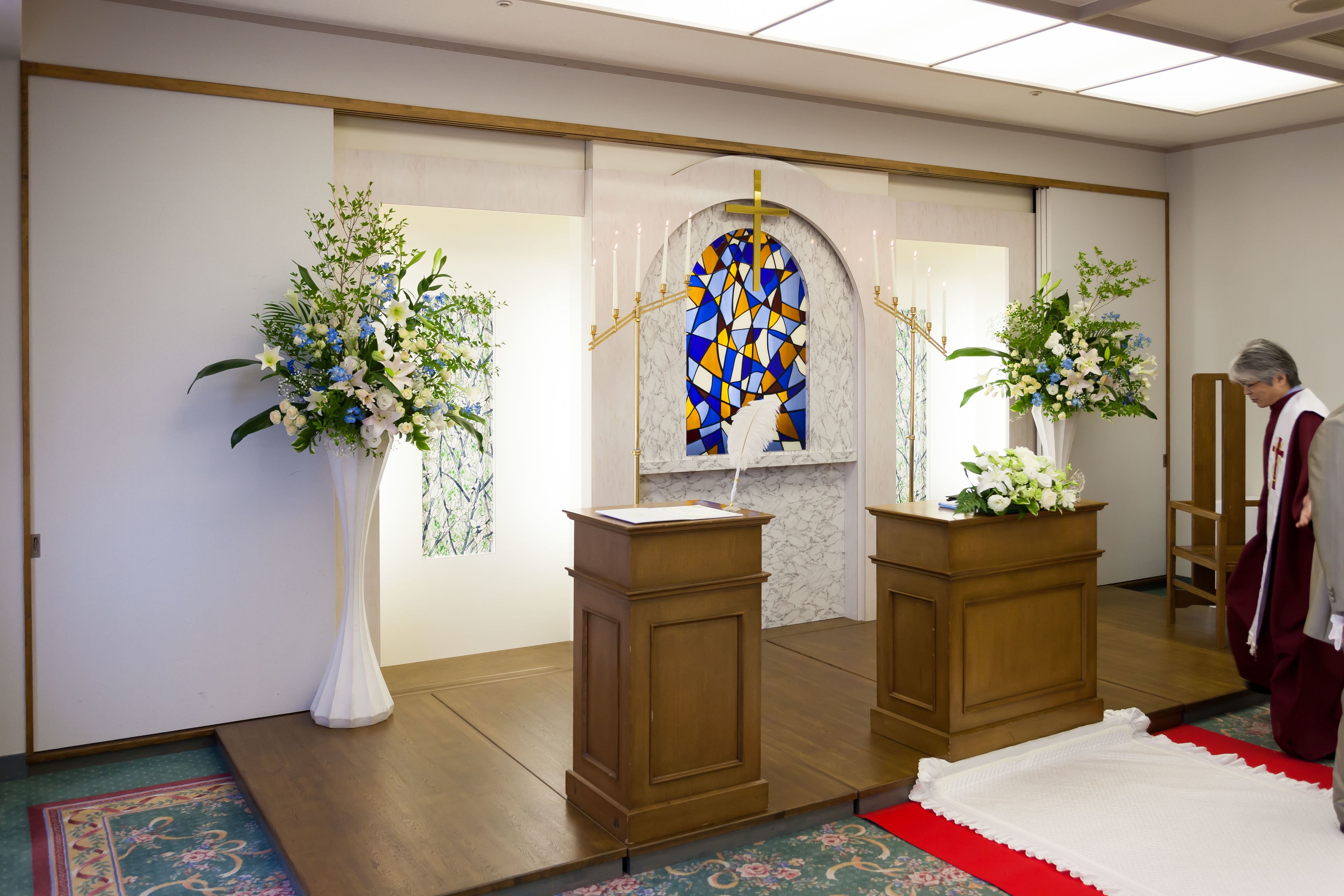 A room with a wooden podium, a stained glass window, and floral arrangements.